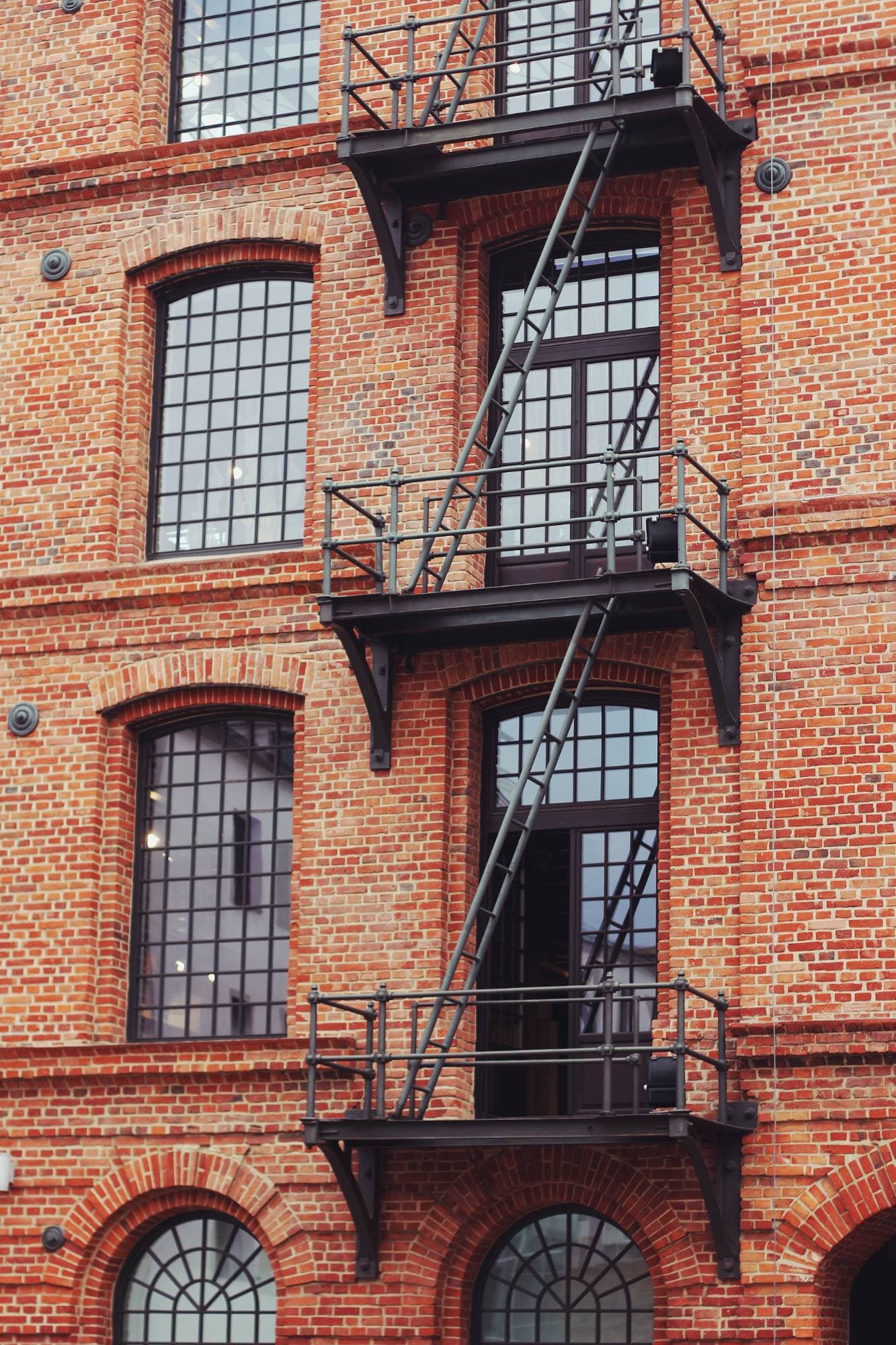 A brick warehouse facade with arched windows and an iron fire escape